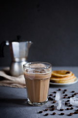 Ice coffee in a high glass, moka coffee maker, a plate of pancakes on a dark gray concrete background, vertical photo