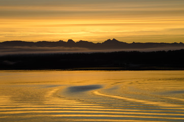 Sunset is reflected in the wake of a cruise ship on the calm waters of the inside passage of Southeast Alaska. - 121289457