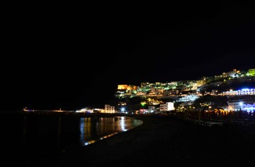 Panorama der farbig beleuchteten italienischen Altstadt Peschici bei Nacht vom Strand aus gesehen