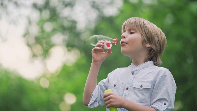 Happy boy blowing soap bubbles outdoors