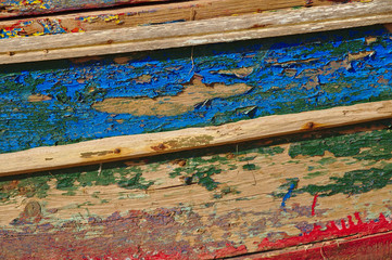 Old and washed out fishing boat hull. Several layers of paint peeling off the wooden surface