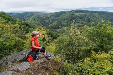 Senior woman sits on a rock and looks into the landscape