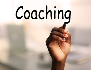 Human hand writing word COACHING at transparent whiteboard on blurred background