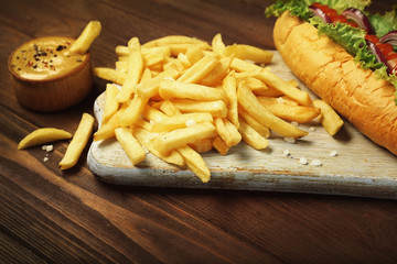 Delicious hot dog and fries on wooden board