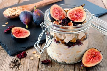 Jar of overnight autumn oats with red figs, cranberries and walnuts against a rustic wood background