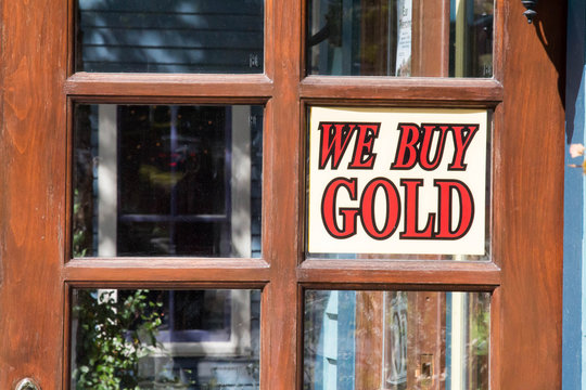 A "We Buy Gold" sign is posted in a shop window pane