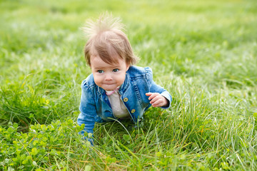 Baby girl crawling on the green grass outdoors in summer