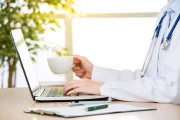 Doctor using computer to research internet and drink coffee