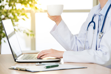 Doctor using computer to research internet and drink coffee