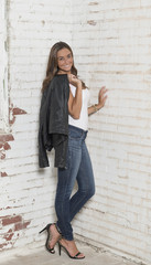 Sexy Caucasian woman in black jacket, white tank-top and blue jeans poses in industrial warehouse studio - fashion model