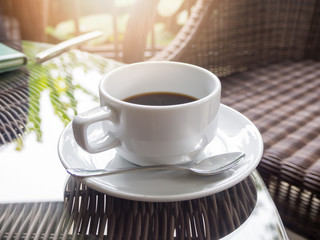 Hot black coffee in white ceramic cup on wooden table.