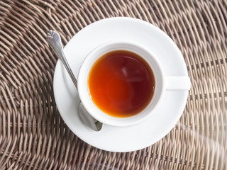 Hot black tea in white ceramic cup on wooden table.