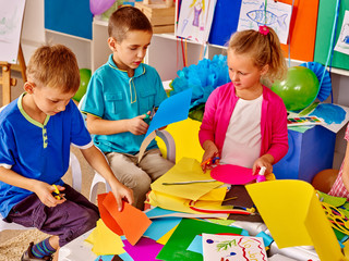 Fototapeta premium Children are making something out of colored paper on table in primary school. Children craft lesson in primary school. Development children craft at class in school. Independent work.