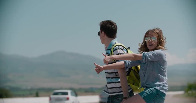 young couple standing on an empty road, hitchhiking, mountainous terrain, slow motion
