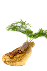 eine schwarze Karotte auf einem Olivenbrett vor weißem Hintergrund