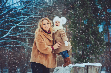 Obraz premium Happy mother and baby daughter walking in snowy winter park. Christmas family time.