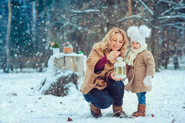 Obraz premium Happy mother and baby daughter walking in snowy winter park. Christmas family time.