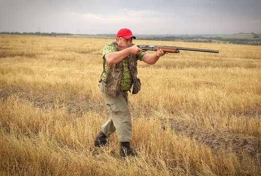 Hunter with a gun on the field aiming at the prey