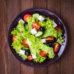 Greek salad (lettuce, tomatoes, feta cheese, cucumbers, black olives) on dark wooden background top view. Healthy food.