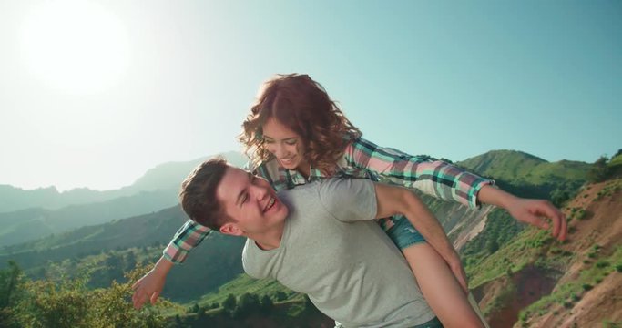 Happy Couple Having Fun Outdoors in the background mountains sunset time,slow motion . Laughing Joyful Family. piggyback. Freedom Concept