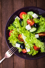 Greek salad (lettuce, tomatoes, feta cheese, cucumbers, black olives) on dark wooden background top view. Healthy food.