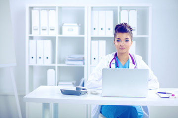 Beautiful young smiling female doctor sitting at the desk and writing.