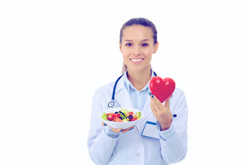 Portrait of a beautiful woman doctor holding a plate with fresh vegetables and red heart