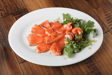 Smoked trout with greens on a white plate. Wooden background.