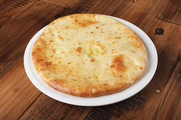 Ossetian pie with mashed potatoes or mutton on a white plate. Wooden background.