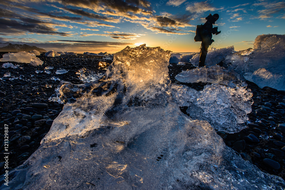 Wall mural Sunrise shot through a gigantic iceberg on black sand beach, Iceland. Iceland Tourist attraction.