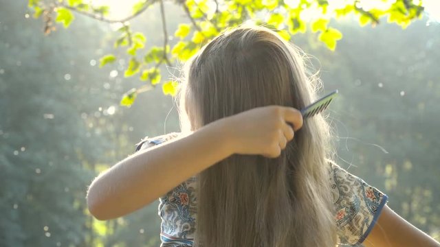 Pretty girl combing her hair sitting in Sunset Light. Close-up. 4K