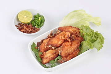 Deep fried chicken topped fried sliced red onion served with side dish as halve green lemon ,minced shallots and filled fried red onion . Side view.