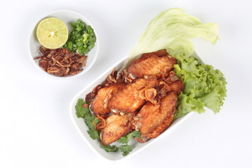 Deep fried chicken topped fried sliced red onion served with side dish as halve green lemon ,minced shallots and filled fried red onion . Top view.