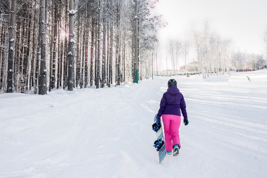 Girl in purple jacket and pink pants with snowboard in the hands