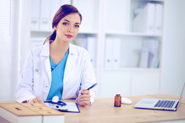 Beautiful young smiling female doctor sitting at the desk and w