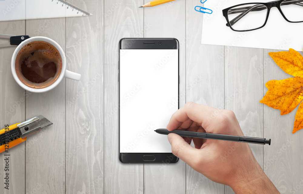 Poster Man writes with a pencil on phone display. Modern smart phone on table and pencil in hand. Isolated display for mockup. Coffee and glasses beside.
