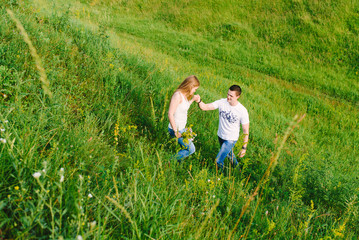Naklejka na ściany i meble Man and woman walking in the park. A nice young couple trying to climb the green grass slope