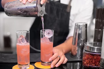 Tuinposter bartender puring sweet pink mocktail on ice in the glass © lmanju
