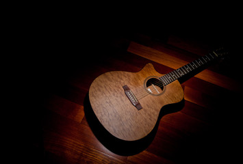 Acoustic mahogany guitar under a spotlight, bottom right of frame