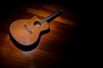 Acoustic mohagony guitar under a spotlight, top left of frame