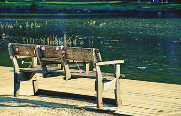 Rustic wooden park bench draped in faded pink party decorations on the bank of an emerald green river. Audley, Royal National Park, Australia
