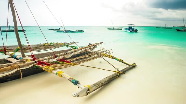 wooden african fishing sailing boat with oars in water near a shore with turquoise ocean and boats on the background, timelapse