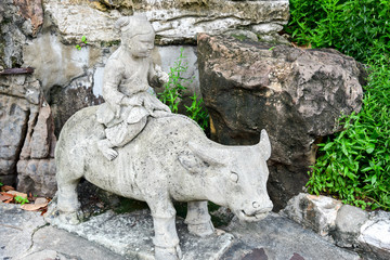 Fototapeta na wymiar Stone Guardian Statue Depicting a Child Riding on a Buffalo at Wat Pho, Bangkok, Thailand