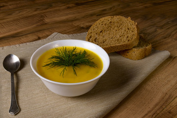 Bowl of pumpkin soup with bread and greens on wooden surface