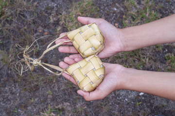 A hand holding Ketupat (Rice Dumpling) - Malay cuisine made from glutinous rice packed inside a diamond shaped container of wooven palm leaf.