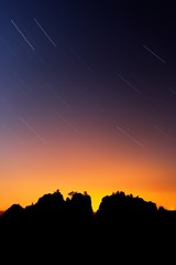 Silhouetted rocks and circumpolar stars. Beautiful night view over sandstone cliff into deep misty valley in Saxony Switzerland, colour background with orange and blue sky star sun on sky, Germany