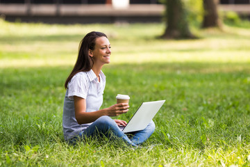 Beautiful businesswoman is drinking coffee and using laptop while resting from work at the park.