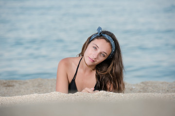 Cute girl with long hair and bow headband lying on the sand