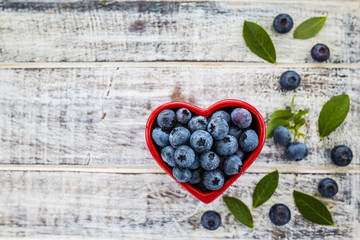 Fresh blueberries in a bowl in the shape of a heart on a wooden background. Space for text.
