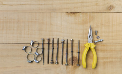Screw and steel pliers on wood background